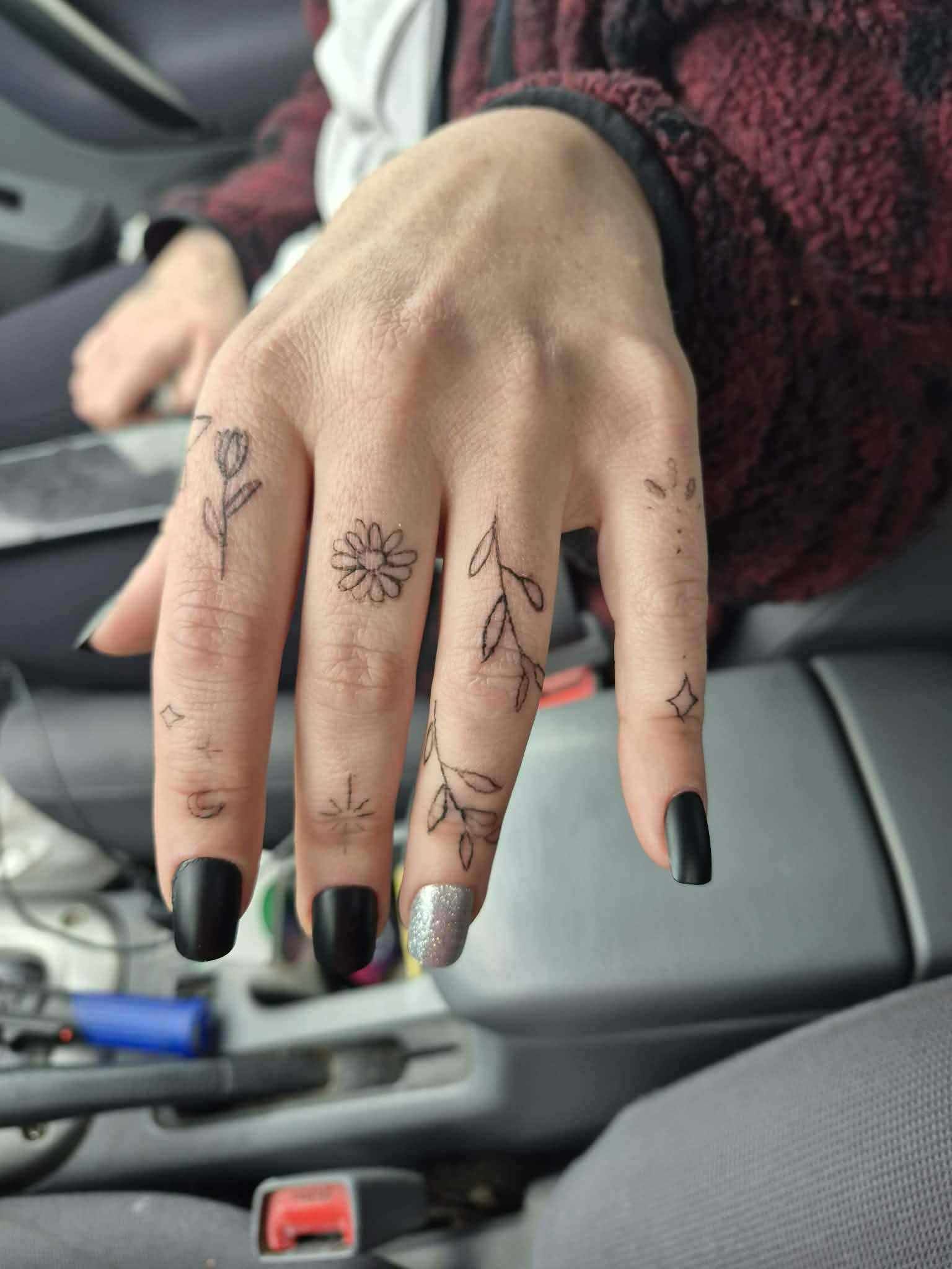Fine line botanical finger tattoos — daisies, vines, stars
